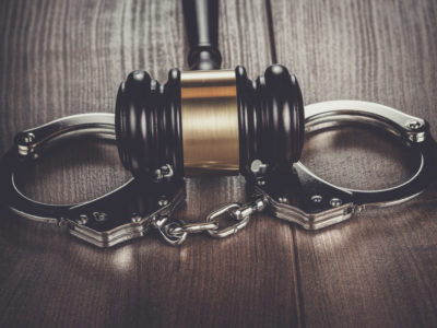 handcuffs and judge gavel on brown wooden table background